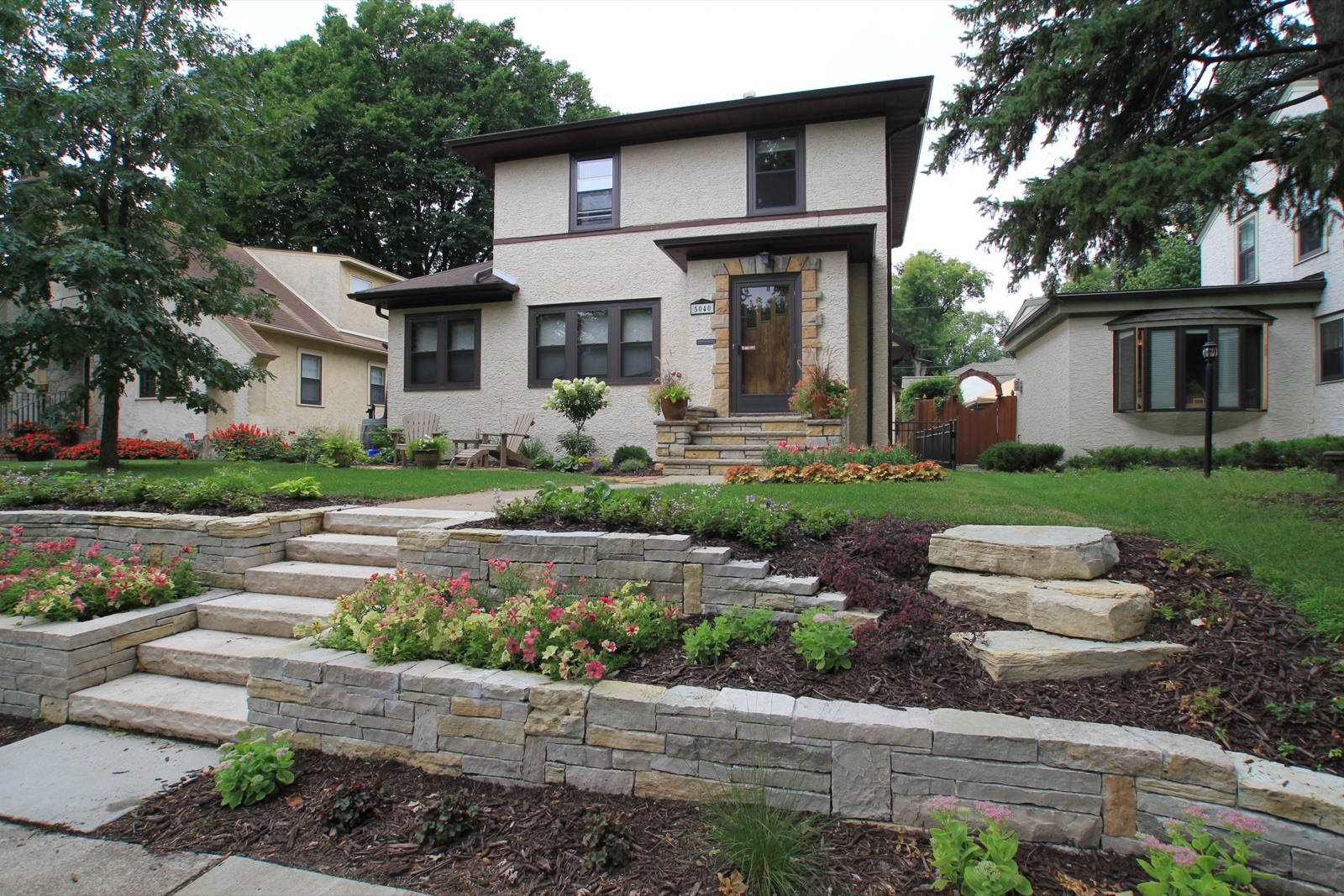 Tiered stone retaining wall, paver steps, and landscaped front yard hardscape in a Rogers neighborhood
